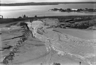 Hietaniemen hautausmaan kivipenger on rakenteille. Taustalla näkyvät Kotkasaaret(Ourit). Iso halli etualalla olevalla saarella on Petterssonin veistämö. Asuintalo hallin vasemmalla puolella on alunperin kalkkiuunin hoitajan talo.  Takana näkyvät O.E. Lindgrenin asuintalo ja veistämö. Foto: Kalle Havas Helsingin Kaupunginmuseo.